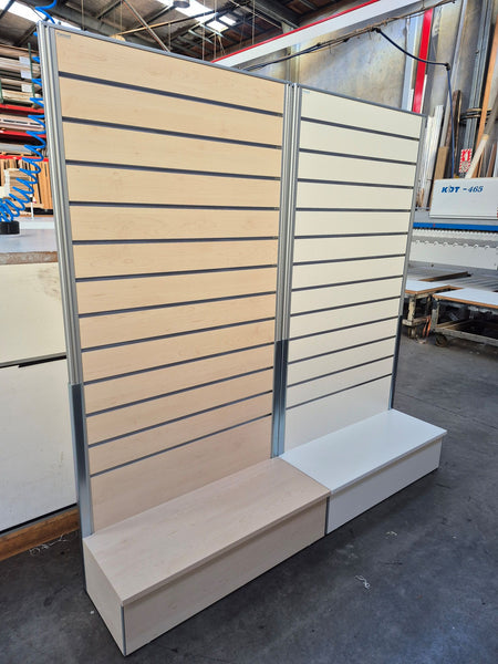 Two freestanding light weight slatwall display panel in a light wood finish in a factory setting
