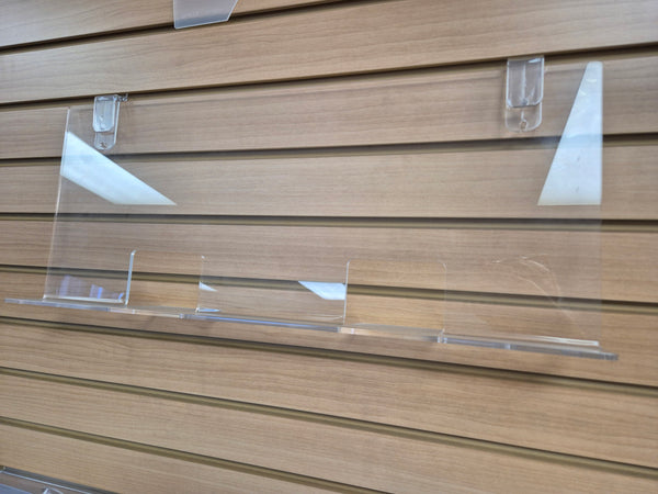 Clear acrylic display shelf with clips mounted on a wooden slatwall display system.