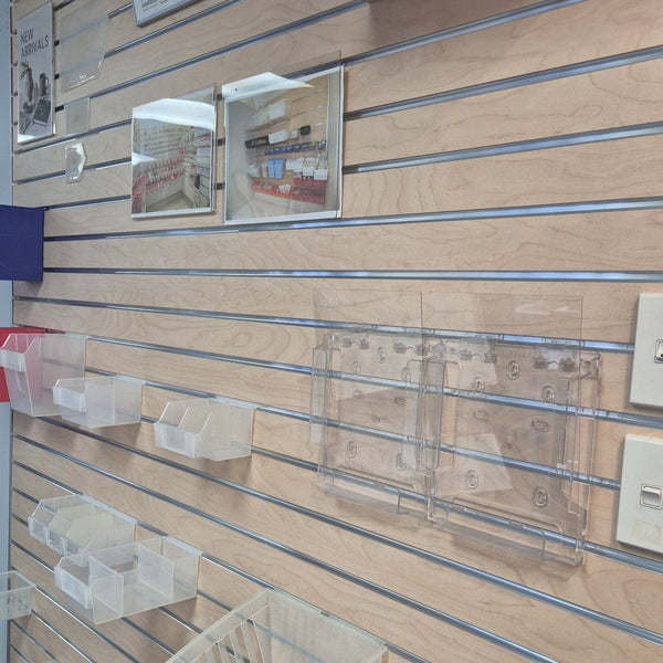 Clear plastic wall-mounted organizer bins and clear acrylic display frames mounted on a light wood slatwall display wall.