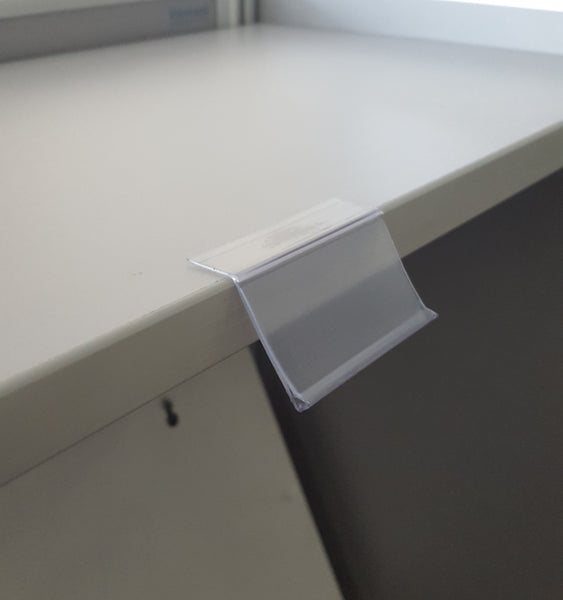 Angled clear data strip (ticket strip) with adhesive backing for NZ retail shelves shown stuck to a shelf.