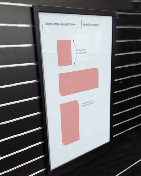 A black snap poster Frame portrait A2 hanging on black slatwall displaying a graphic design poster