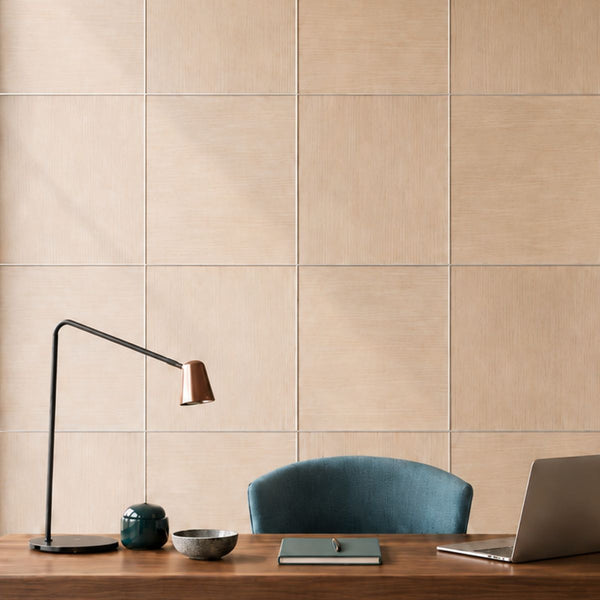 Beige wood-look wall panels arranged in a grid separated by MCBUT butt join aluminium profiles behind a wooden desk with a black desk lamp, a blue chair, a notebook, and a laptop.