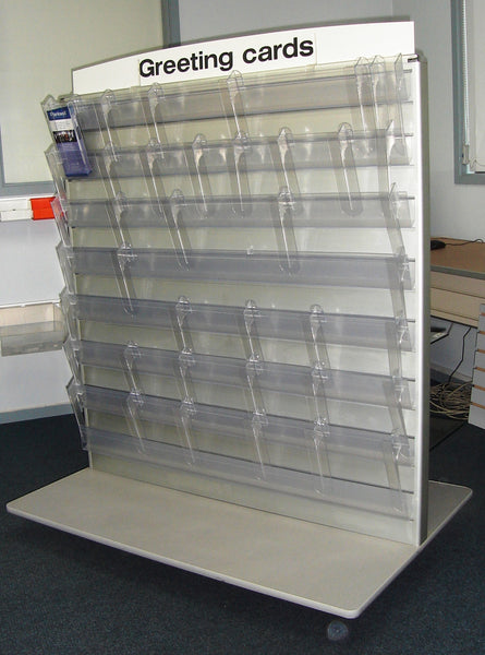 Photo of a Calext clear plastic modular print display system mounted on a slatwall gondola with empty shelves and a Greeting Cards header card.