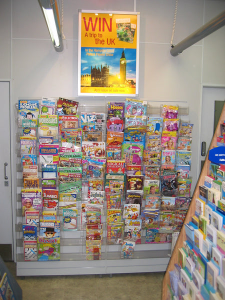 Display of magazines shown wall- mounted with the Calext modular magazine display system with a promotional poster above in a retail store.