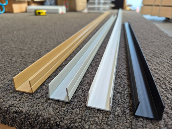 EC18 PVC Panel Capping profiles for 18mm panels (shown concave) in close up in a factory setting showing the range of 4 available colours: Tawa, White, Light Grey and Black