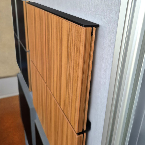 Close up of a Stickman aluminium MCLNWFCAP wall fix capping profile powder coated black flush set capping walnut MDF panels showing the gap coverage to the back wall. 