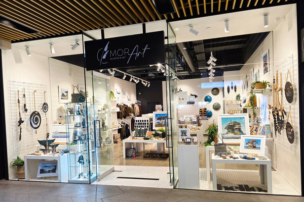 Storefront of Mor Art with various art pieces displayed inside on Plankwall nesting tables, plinths and white slatwall panels.