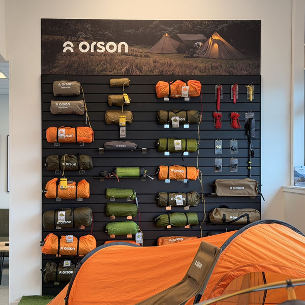 Orson camping gear displayed on black 100m pitch slatwall wall panel with black inserts with a tent in front of it.