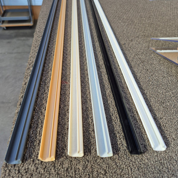 Close up of Plankwall Slatwall J inserts in a range of 6 colours, grey, tawa, cream, grey, black and white in a factory setting