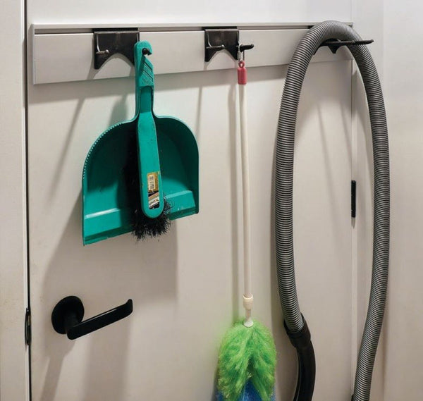 Cleaning tools including a green dustpan and brush, a duster, and a vacuum hose hanging on hooks against a white door.