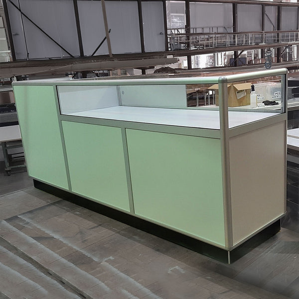A white retail counter unit with a large glass display counter top in a factory setting - front view