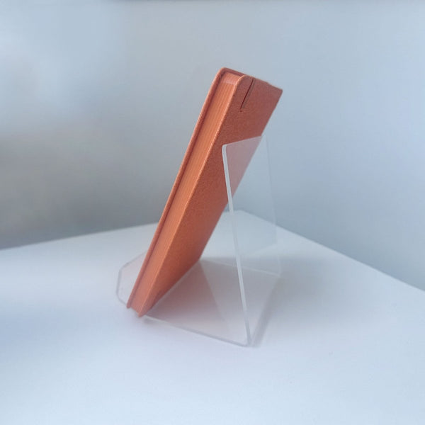 Copper-colored book on a clear easel display stand against a white background