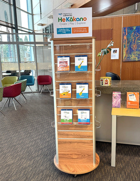 Plankwall wooden display rack with books and a 'He Kākano' sign in a modern office setting.