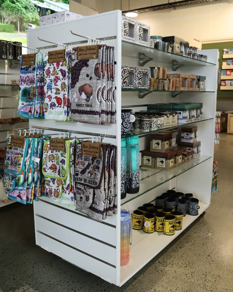 Plankwall slatwall display gondola lightweight with glass shelves in white merchandised with tourist products in a retail setting.