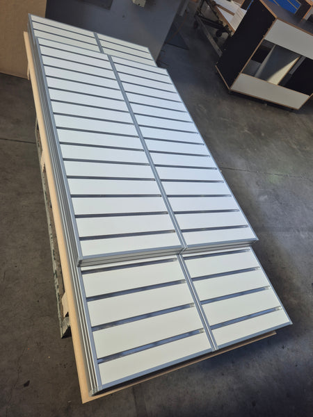 Plankwall EP18 aluminium capping shown capping white 18mm slatwall panels shown stacked on a concrete floor in a factory 