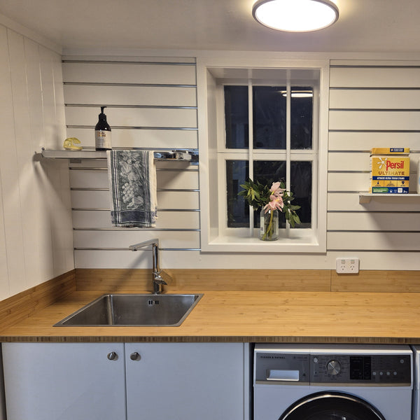 Modern laundry with slatwall wall including Plankwall hanging rail with a built in shelf, wooden countertop, sink, and window with plants.