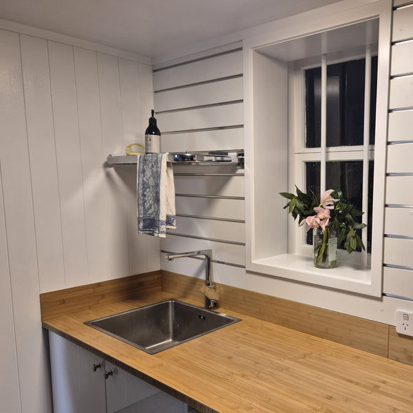 Modern laundry corner view with slatwall wall including Plankwall hanging rail with a built in shelf, wooden countertop, sink, and window with plants.