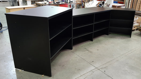 Plankwall L-shaped retail counter and reception desk back with open shelving  in a warehouse setting with various items in the background