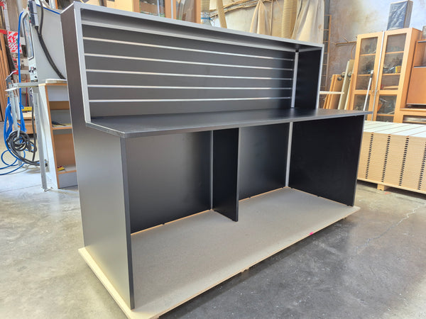A photo of a Plankwall Reception Desk, 1800mm wide in Black shown in side view in a factory setting