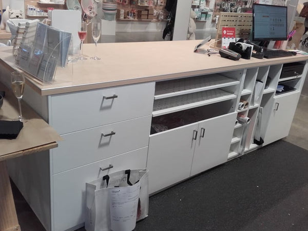 White retail counter top with storage cabinets and a computer setup in a store setting