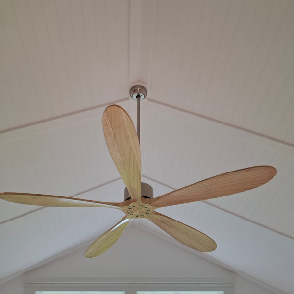 Ceiling fan with wooden blades against a W Grooved white ceiling.