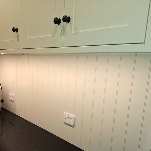 Wall with W grooved MDF painted white with green cabinet above it with black knobs