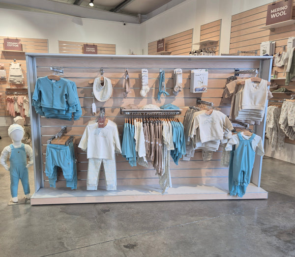 display of kids clothing merchandised on a slatwall gondola in walnut wood and white ply in the middle of a retail store. 