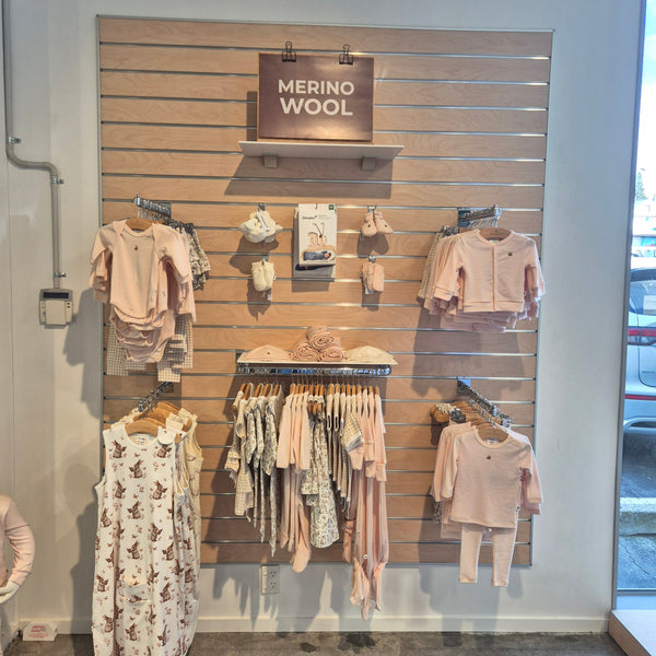 Slatwall panel in blonde wood affixed to a store wall displaying baby clothes on shelves and different brackets