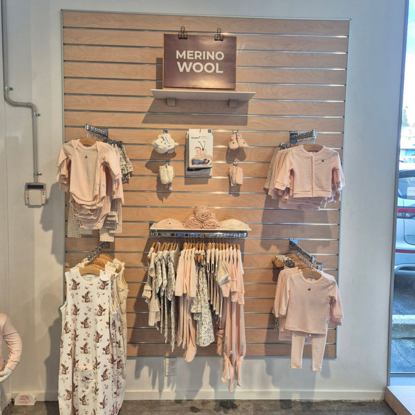 Slatwall panel in blonde wood affixed to a store wall displaying baby clothes on shelves and different brackets