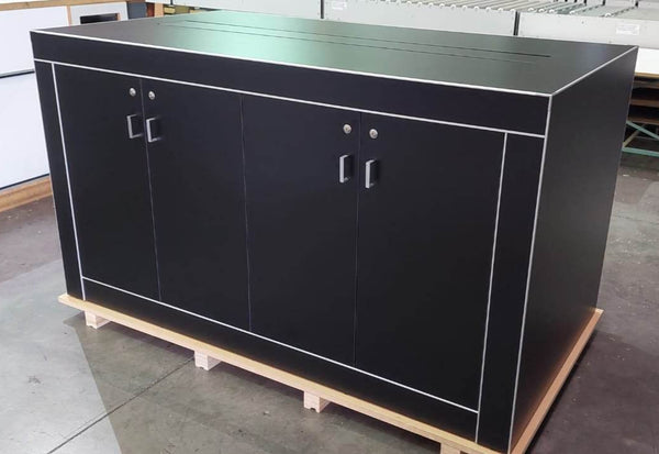 Photo of a black custom electronics display table with a central cords console and lockable cupboards in a factory