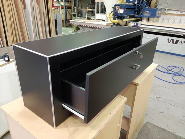 Plankwall custom low single lockable drawer cabinet in dark wood with aluminium edging in a factory setting.