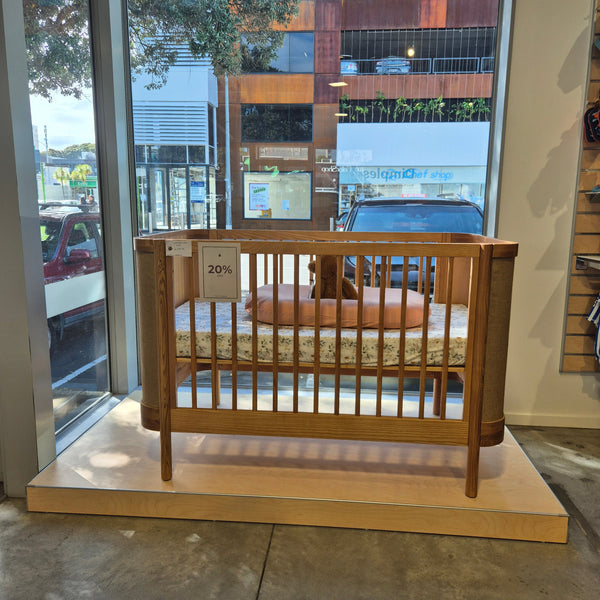 a baby bed displayed in the window of a baby store merchandised on a blonde wood floor stock retail plinth with a city street in the background.