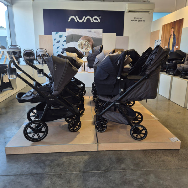 A group of retail floor stock low plinths in blonde wood finish displaying baby buggies in a retail store.