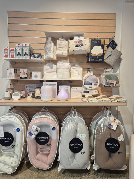 Array of baby accessories merchanised on shelves, including strong heavy duty shelves mounted on a slatwall panel in blonde wood in a retail store.