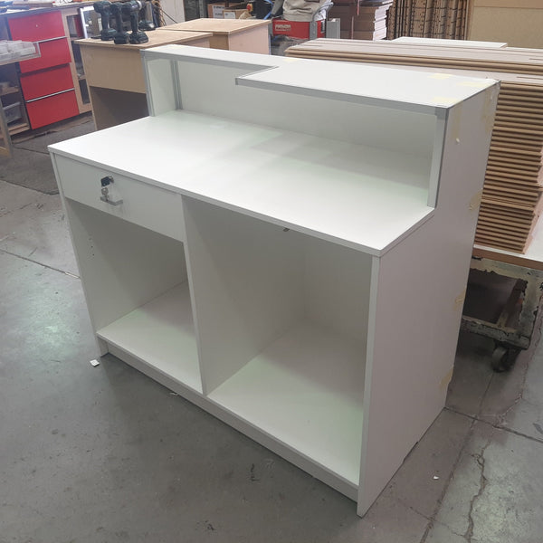 Plankwall cashier desk retail counter in white with raised front section, lockable drawer and shelves. back view  shown in factory setting