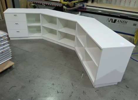 White L-shaped reception desk  retail counter in a warehouse setting with shelving and drawers