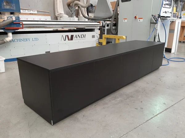 Plankwall custom low cabinet with five concealed opening drawers in dark wood in a factory setting.