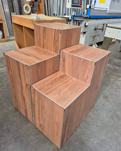 Set of 4 cube retail display stands in a woodgrain finish shown grouped together in a factory setting