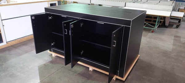 Photo of a Plankwall electronics detail retail display table in black showing lockable storage cupboards open underneath the table shown in factory