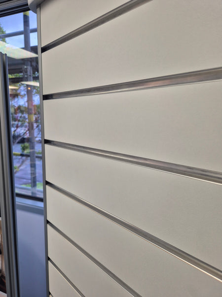 Close-up of a white horizontal slatwall panel with aluminium inserts besides a window.