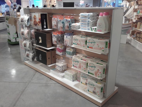 Display of baby products including diapers and bottles merchandised on a maple wood and white ply display gondola in a store setting.