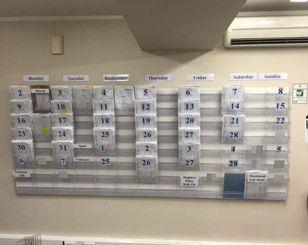Weekly project schedule and work notes shown organised in a Calext wall-mounted modular print display system.