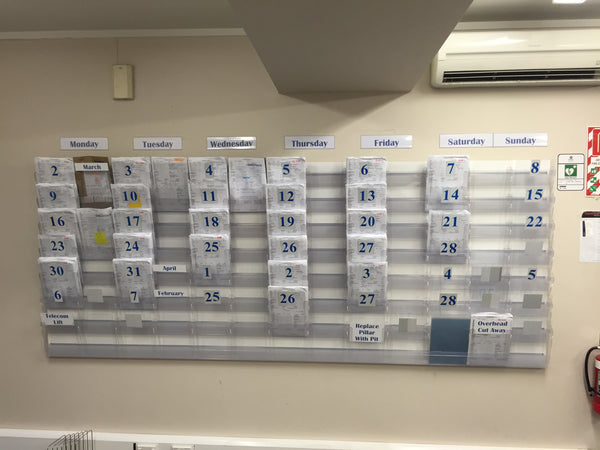 Weekly project schedule and work notes shown organised in a Calext wall-mounted modular print display system.