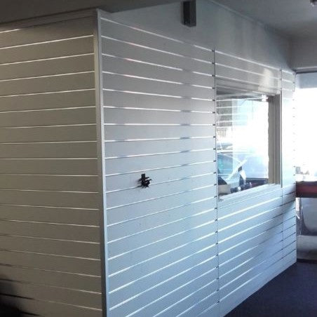 White slatted partition wall panels with a window and a small black hook, shown in an indoor setting.