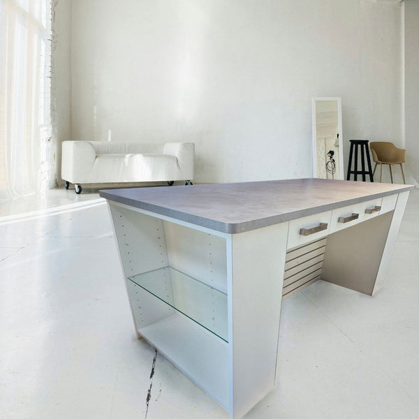 Plankwall retail counter in white with a stone top, glass shelf on the side, drawers in the back and slatwall hanging space underneath on a white background.