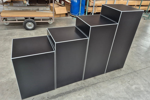Set of 4 black cube retail display stands stacked in a line in a factory setting