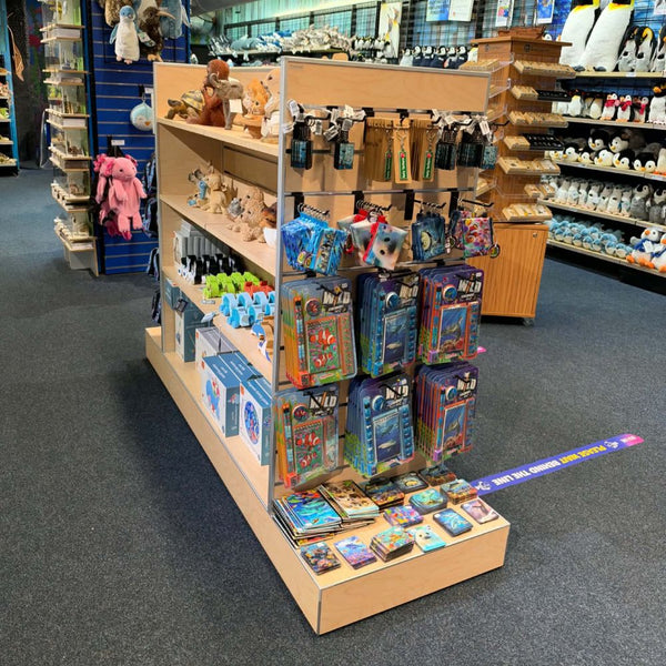 A Plankwall wooden slatwall retail display stand filled with assorted merchandise, including packaged toys, keychains, and small boxed items, photographed inside a store. Other store shelves with plush toys and products are visible in the background.