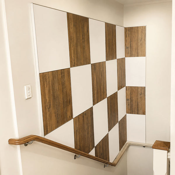 A staircase landing wall decorated with a checkered pattern of white and medium brown wood-look panels created with MCLN Stickman Linear Butt  Join and MCLNCAP Capping aluminium profiles featuring a wooden handrail along the bottom.