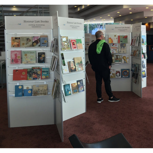 Person browsing books at a book fair with Plankwall 3 way radial display stands on either side.