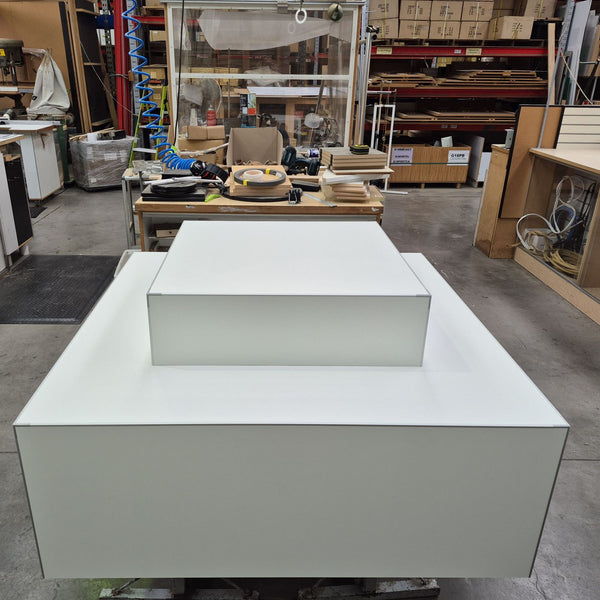 two tier retail display plinth in white shown in a factory setting